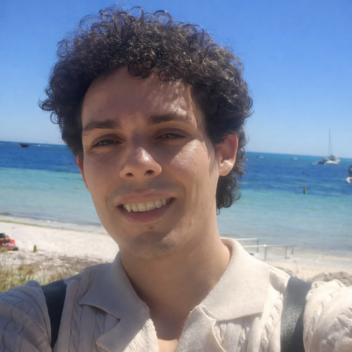 Leonardo Albuquerque de Abreu smiling at the beach, with clear blue ocean and boats in the background